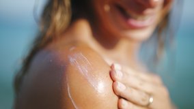 Close up of a happy smiling young woman is applying a sunscreen or sun tanning lotion on a shoulder to take care of her skin on a seaside beach during holidays vacation. - Powered by Shutterstock - Get 15% off with code: PIKWIZARD15