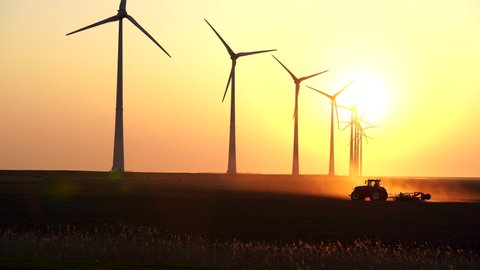 A tractor cultivating farmland during sunset at a row of windturbines. Groningen, Holland.