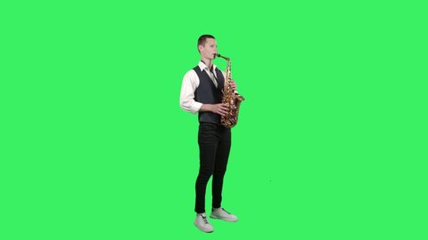 Portrait stylish young guy plays melody at saxophone on a green screen in the studio. Saxophonist performing a solo. Side view.