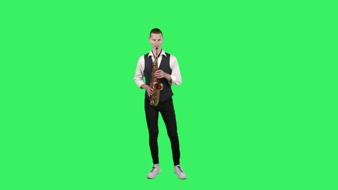 Portrait stylish young guy plays fast melody at saxophone on a green screen in the studio. Saxophonist performing a solo.
