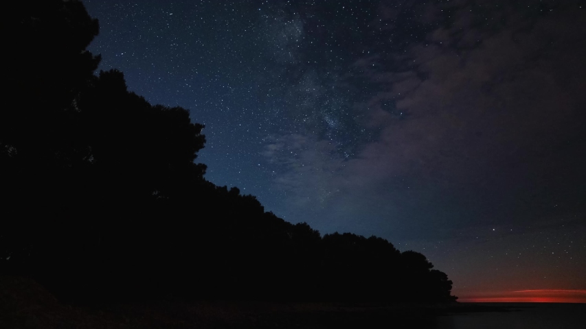 Beautiful time-lapse of the European summer night sky and the Milky Way with thousands of stars and seen from a beach in Croatia with some last hints of daylight at the horizon and ships passing by.