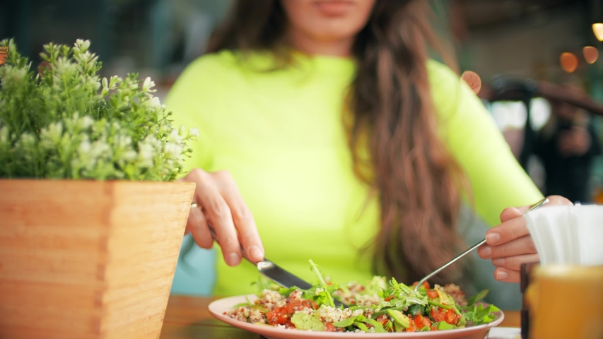 Unknown beautiful young woman eats vegetarian salad in a cafe. Healthy eating concept