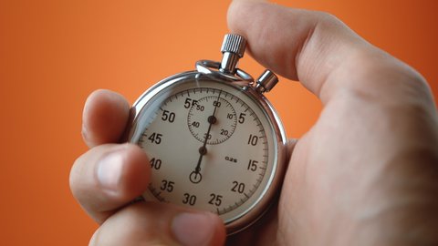 Male hand holding analogue stopwatch on orange color background. Time start with old chronometer man presses start button in the sport concept. Time management concept.