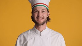Attractive cheerful italian chef in uniform holding tomatoes and macaroni joyfully looking in camera over colorful background