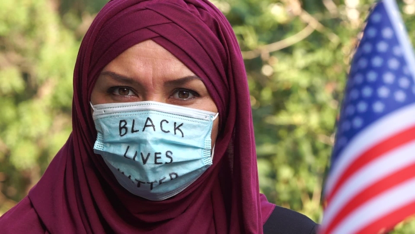 Black Lives Matter (BLM) movement in the United States. A Muslim woman in a hijab with the the slogan is written on the mask. Islam in America Royalty-Free Stock Footage #1056694646