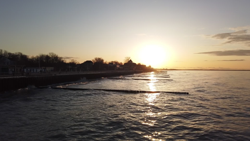 Seafront of the inclement Baltic Sea with stormy waves rolling on wooden piles under cloudy sunset sky on a cold winter day
