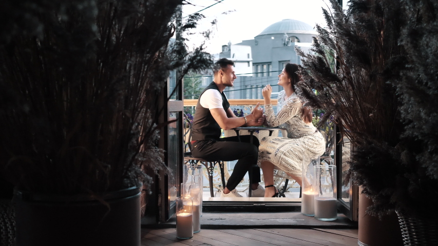 Romantic Date of Young Affectionate Laughing Couple Holding Hands Sitting on Restaurant Balcony Face to Face Indoors. Happiness, Joy Moment, Love Feelings of Two Funny Lovers Enjoying Evening Together Royalty-Free Stock Footage #1056696569