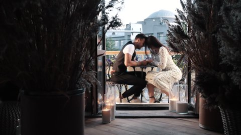 Romantic Date of Young Affectionate Laughing Couple Holding Hands Sitting on Restaurant Balcony Face to Face Indoors. Happiness, Joy Moment, Love Feelings of Two Funny Lovers Enjoying Evening Together