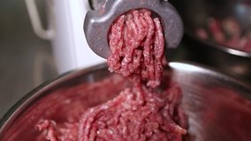 Meat mincer machine chops uncooked red beef steak into patty for hamburgers in close up video clip.Kitchen equipment mincing steaks in closeup footage.Preparing raw mincmeat in butcher shop 