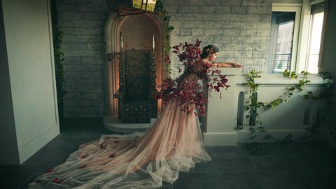 Beautiful young fantasy woman in image magic fairy princess. Elven Queen stands in ancient medieval room. Creative costume red butterfly. beige peach luxury fairytale dress, long lush train plume
