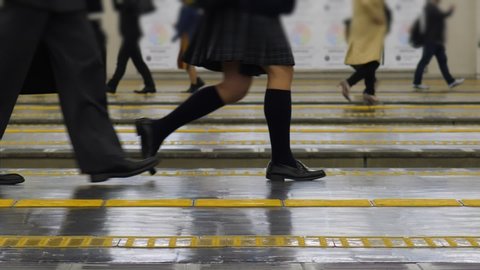 Schoolgirl and office man walk at railway station platform, slow motion shot of legs. Japanese commuters come to train at end of weekday. Passengers seen on background