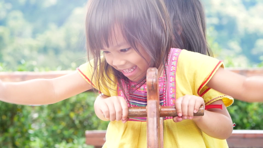 Happy sibling sisters playing with wooden rocking horse in the park. Concept of happiness in childhood.
