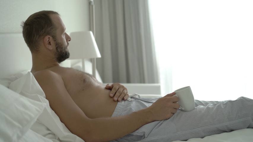 Young man drinking coffee and relaxing while lying on bed at home