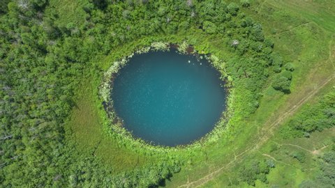 Aerial top down hyperlapse amazing lake of round shape. Cloudy sky reflected in clear turquoise water of pond surrounded by trees and plants. Ripple on water surface, windy sunny summer day