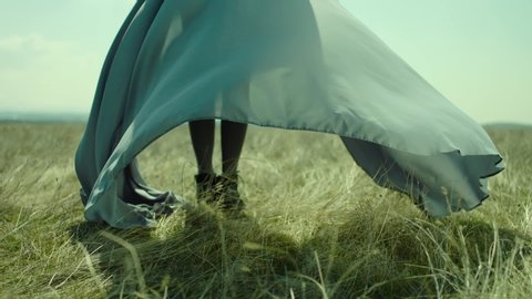 Rear view of woman's leg standing on field . Young stylish lonely girl stay on meadow field . Long skirt fabric flowing by wind in slow motion . Fashion style . Shot on ARRI Alexa Cinema Camera