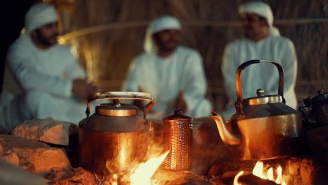 Three arab men in dish dash sitting around the bonfire with tea pots on fire