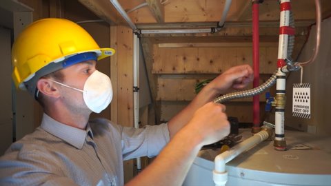 Man wearing mask and helmet back to work and inspecting a hot water heater