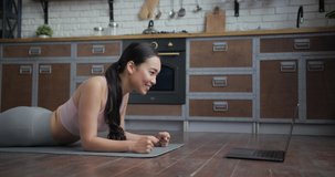 Healthy Asian yoga woman standing in plank with online trainer using laptop
