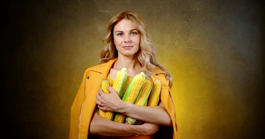a woman in a yellow jacket holds a freshly picked ear of corn in her hands