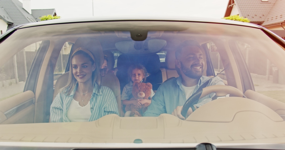 Front view of happy loving parents and their excited kids speaking smiling driving car in city. Young family traveling abroad by car in summer. Concept of lifestyle, happy family, travel together. Royalty-Free Stock Footage #1056731837