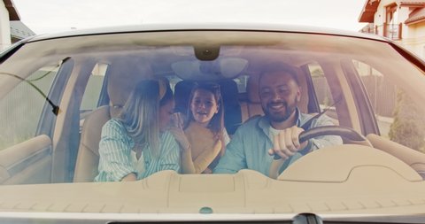Front view of happy loving parents and their excited kids speaking smiling driving car in city. Young family traveling abroad by car in summer. Concept of lifestyle, happy family, travel together.