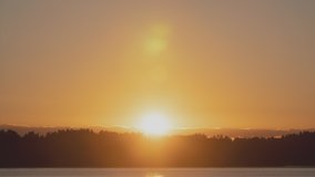 Time-lapse sunrise over beautiful lake. Water surface in fast motion. Warm sky with rolling clouds. Trees silhouette woodland on horizon. Early morning shot in timelapse. Bright sun rises over skyline - Powered by Shutterstock - Get 15% off with code: PIKWIZARD15