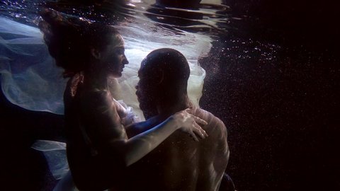 man and woman are having sex underwater in dark depth of pool, brawny man is embracing girlfriend
