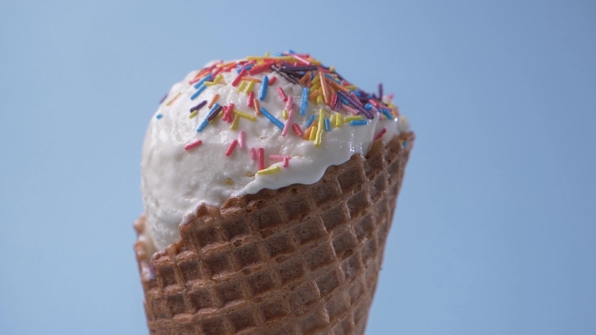Rotating vanilla white ice cream in waffle cone covered with rainbow sugar sprinkles topping on blue background. Sweet dessert. Delicacy. Royalty-Free Stock Footage #1056735938