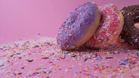 Colorful appetizing tasty donuts with various glazing toppings falling on pink surface with sugar sprinkles. Delicious baked sweet buns. Confectionery.