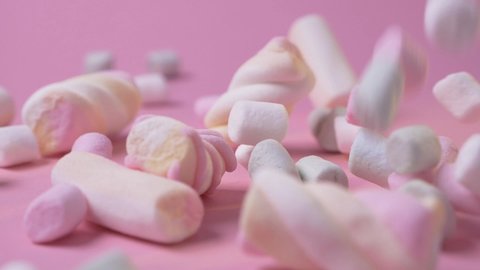 Pink and white mini marshmallows falls on pink background food light sweet dessert candy delicious sugar slow motion