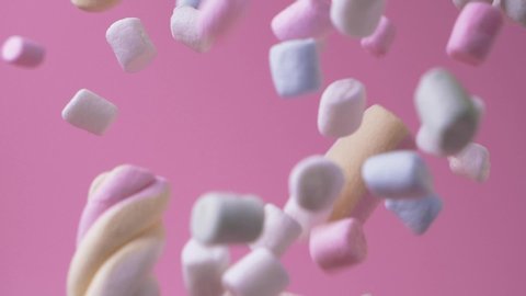 Close up pink and white mini marshmallows falls on pink background food light sweet dessert candy delicious sugar slow motion