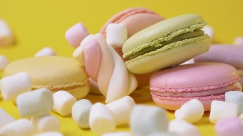 Nice delicious creamy colorful freshly baked macaroons lying on yellow background with fluffy marshmallows falling down. French luxury dessert. Sweet cookies. Sweet-shop.