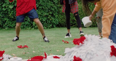 Diverse group of friends celebrating end of COVID-19 quarantine, picking up treats and toilet paper from destroyed coronavirus shaped piñata. Shot on RED cinema camera in slow motion