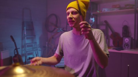 Handheld portrait shot of cheerful young adult man wearing casual outfit enjoying playing drums in his garage studio : vidéo de stock