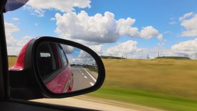 Video shooting in motion, view in the rearview side mirror of a car, driving a red car along the road