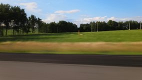 Video shooting in motion, the car drives along the highway along the roadside in the countryside, trees and fields