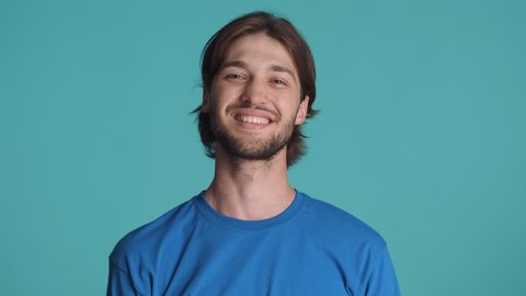 Handsome smiling brunette guy happily showing thumbs up gesture on camera over colorful background. Well done expression