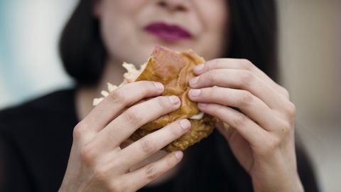 Grabbing a bite to eat. A woman takes a big bite out of a fried chicken sandwich on a restaurant patio. Shot in slow-motion and in 4k. 