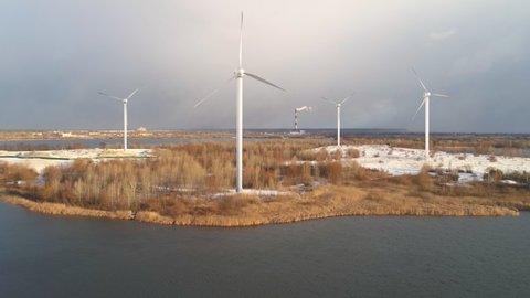 Wind farm on winter island concept. Windmills, clouds, water and snow. Alternative green energy. Sunny day.