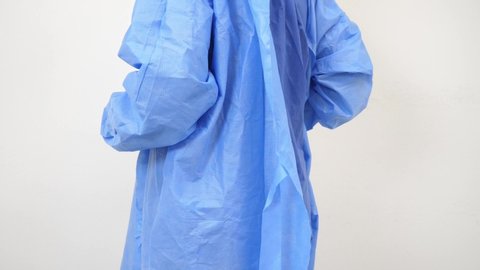 tying blue medical gown up in a white room.
