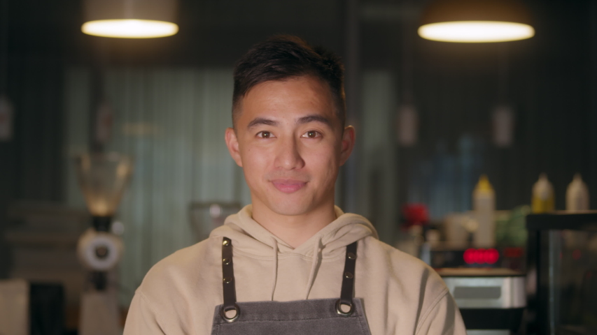 Successful small business korean owner man standing with crossed arms with employee in background preparing coffee. Portrait of asian young male cafe owner . Royalty-Free Stock Footage #1056752903