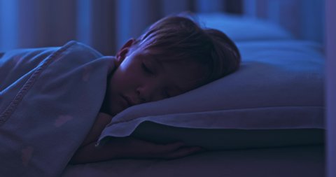 8 years old boy sweetly sleeping in his crib. Face close-up of a sleeping child on its side. Tracking shot of a sleeping kid at midnight. Relax and resting. 4k footage  of a sleeping child in bed.  