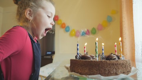 A child blows out the candles on the big delicious chocolate cake. Cute little girl's birthday. A child makes a wish on his birthday. Quarantine and self-isolation