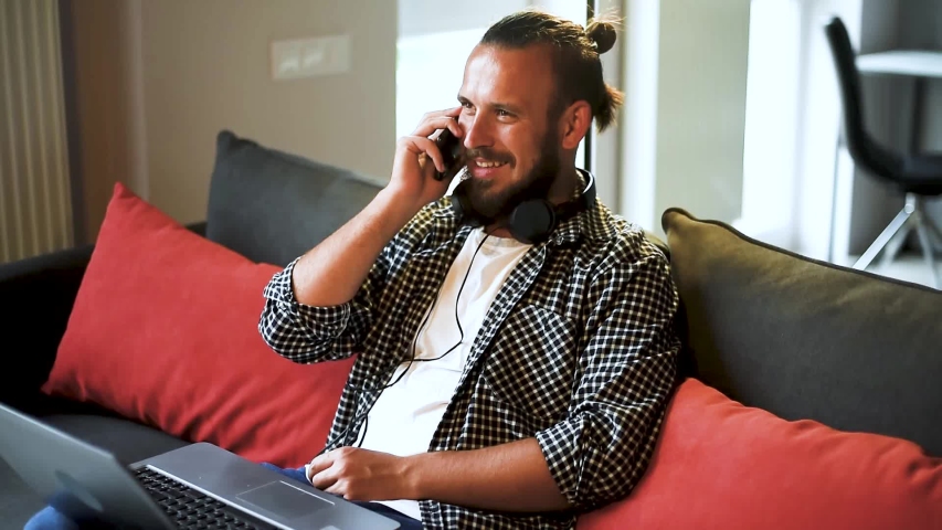 Handsome young man laughing while taking a phone call in his living room.