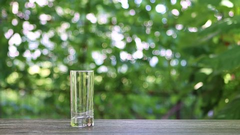 milk is poured from a glass jug into a transparent glass in the summer garden slow motion