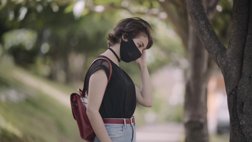 Middle shot of a teenager waiting for her friends in the park, wearing a black mask. Girl uses her phone as a mirror