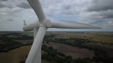 4K drone closeup of a green technology wind turbine on a cloudy day with green grass for epic aerial view.  Moody, majestic clouds seen in the wide shot on this Texas wind farm for renewable energy.