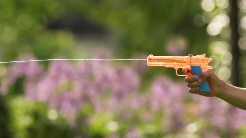 Summertime scene: hand of young Caucasian boy squirting plastic orange toy water gun in garden, close up profile