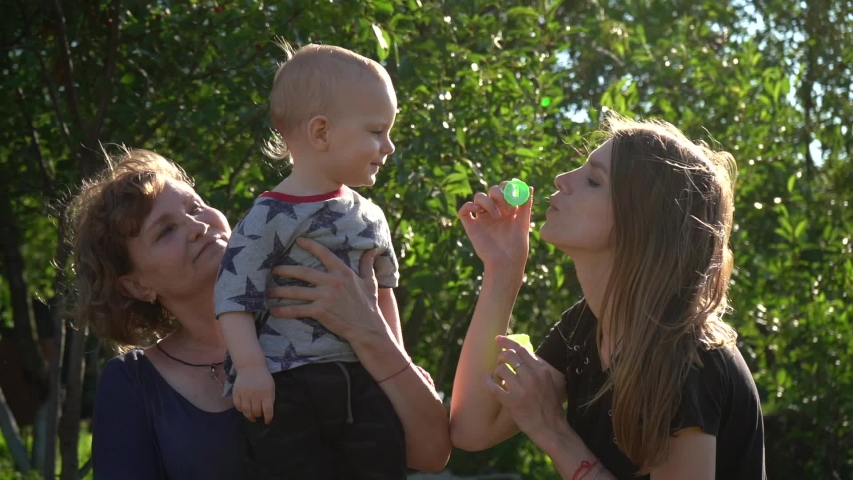 Slow motion. Mother and grandma playing with little boy, bowing soap bubbles