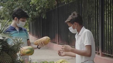 A young male man wearing a protective face mask buying purchasing fruits from a street vendor amid coronavirus  COVID 19 epidemic or pandemic